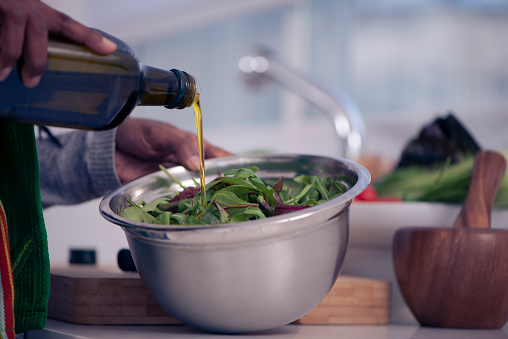 Close up image of woman's hand pouring olive oil to fresh mangold salad.