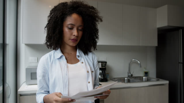 Black woman at home reading the mail looking surprised and serious