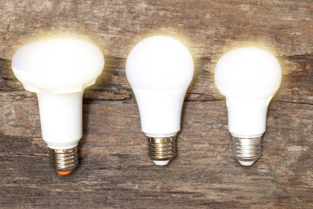 istock Power saving concept. Asia man changing compact-fluorescent (CFL) bulbs with new LED light bulb. 1211663910