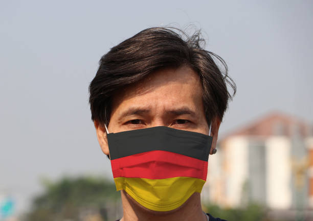 istock Germany flag on hygienic mask. Masked Asian man prevent germs. 1211685472