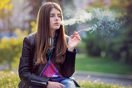Nostalgic young girl is smoking cigarette in the park
