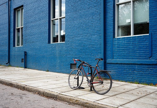 A bike with red trim is locked up on a city sidewalk with a dramatic blue building in the background.