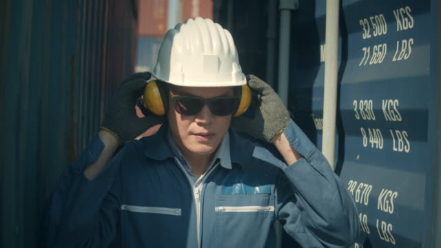 Male worker putting on safety ear muffs to prepare before work in shipping port,Slow motion