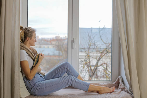 istock Beautiful young girl sitting on a windowsill with a book 1211706460