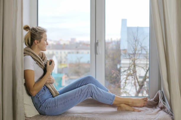 istock Beautiful girl reads a book while sitting on a windowsill and dreams 1211706463