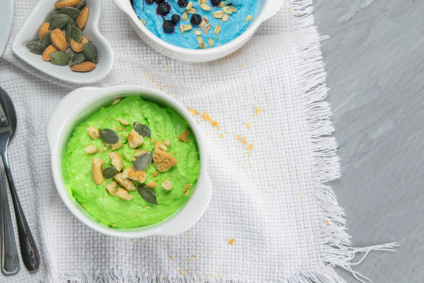 Two curd desserts: one with blueberries and nuts and the other with avocado and kiwi, next to there are pumpkin seeds and nuts