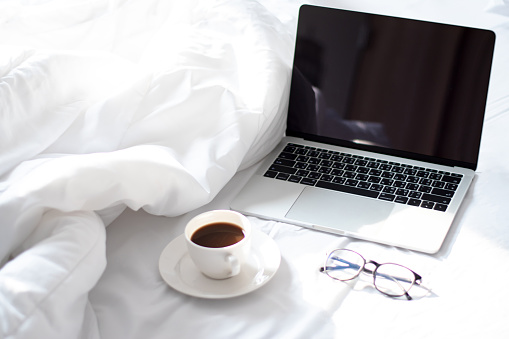 Freelance workspace with hot coffee and laptops with soft morning light on the white bed in the room.