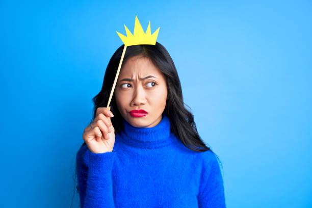 istock Young thoughtful woman with paper crown on stick looking away expressing doubt 1211711659