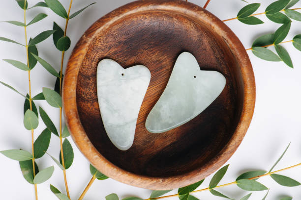 vista dall'alto delle pietre di giada gua sha in ciotola di legno su rami su bianco. - spooning foto e immagini stock