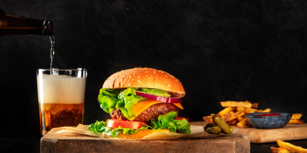 burger and beer panorama. hamburger with beef, cheese, onion, tomato, and green salad, a side view on a dark background with copy space. selective focus - salad food and drink food lettuce imagens e fotografias de stock