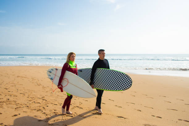istock Couple of surfers walking on beach 1211720546