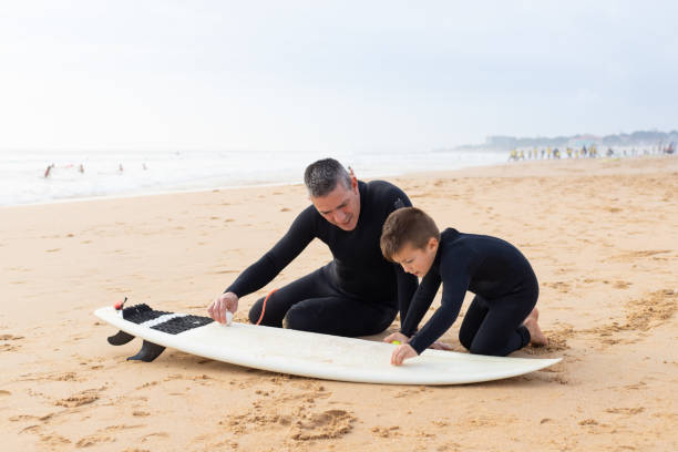istock Father and son waxing surfboard on sand 1211724895