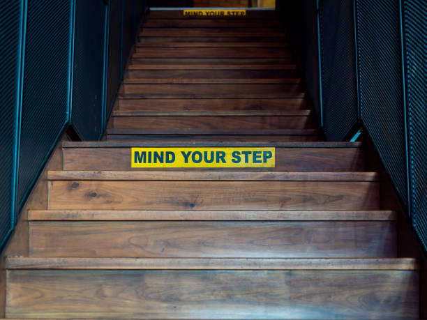 istock Mind Your Step, black text on yellow warning sign on wooden staircase. 1211725652