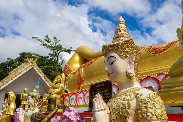 mae hia, chiang mai, norte da tailândia em septemmber 13,2019:a figura de uma deva apertando as mãos em sinal de adoração em frente à estátua de buda reclinável em wat phra that doi kham. - golden temple - fotografias e filmes do acervo