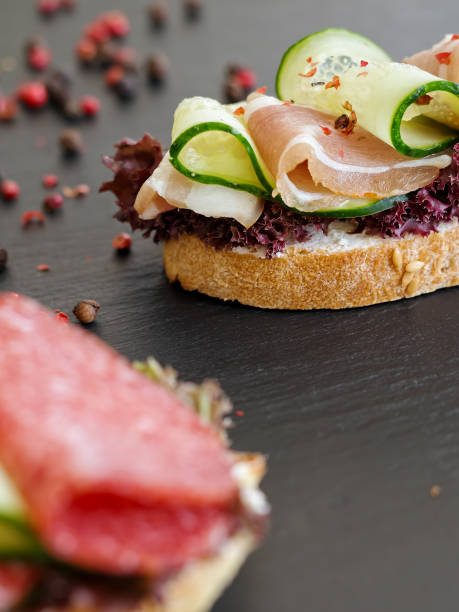 istock Sandwich with bacon cheese, lettuce and cucumber. Quick breakfast. Black stone background. On the back side grains of peppers. Blurred foreground. Close-up. 1211731242