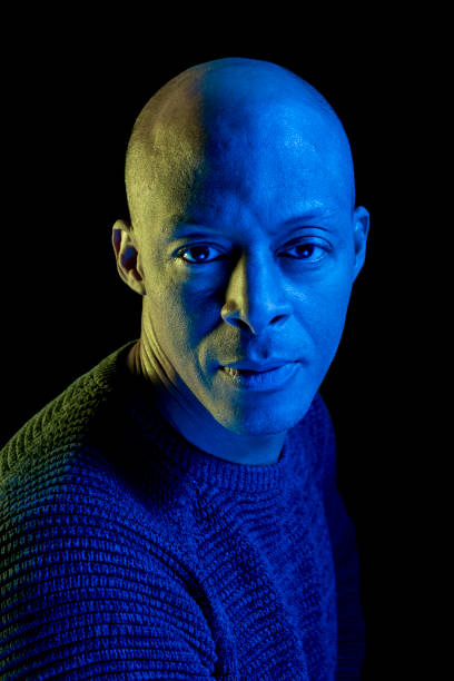 istock Bald black man with blue and yellow light, isolated on black background, looking at the camera 1211731939