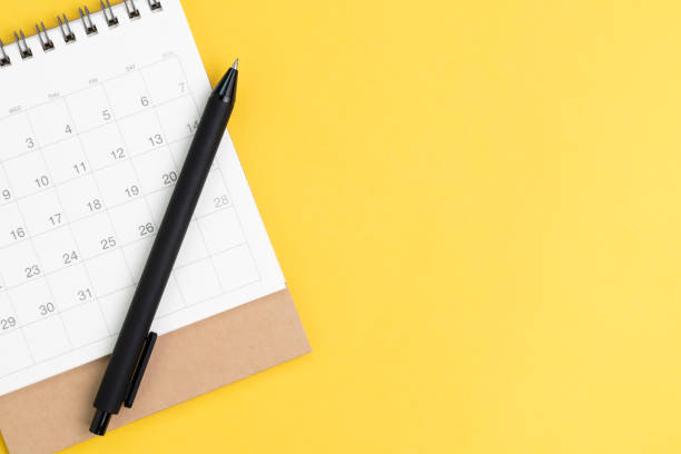 istock Black pen on desktop calendar in flat lay or top view on yellow background with copy space using as writing plan, circle on important day and event or appointment concept 1211739139