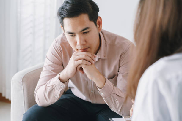 paziente asiatico maschio con psicologa donne che visitano la consulenza e la psicoterapia da parte del medico in clinica. concetto psichiatra - doctor emotional stress worried healthcare and medicine foto e immagini stock