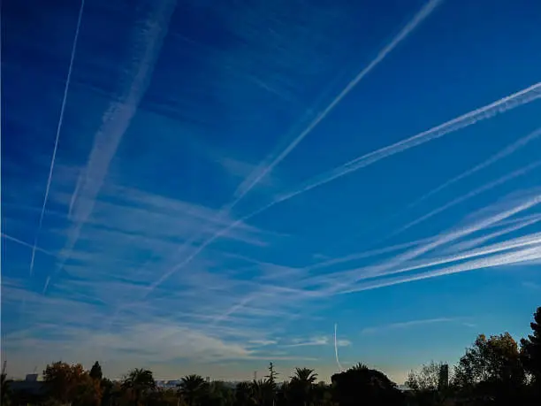 Airplane chemtrails over the trees in blue sky with clouds