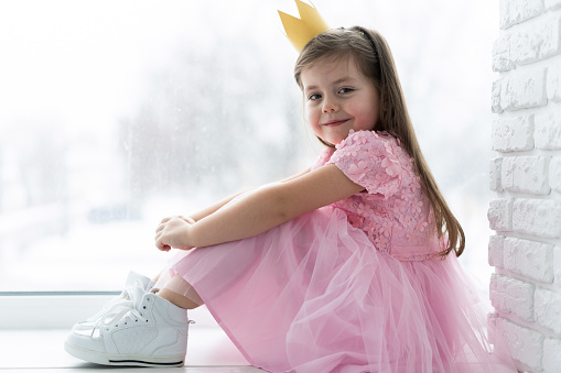 Cute little girl in a princess costume. Pretty child preparing for a costume party. Beautiful queen in gold crown