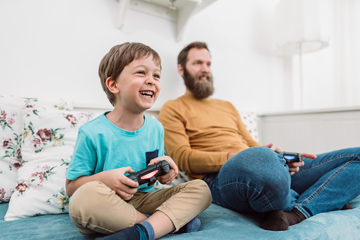 Cheerful little boy playing video games with his father at home
