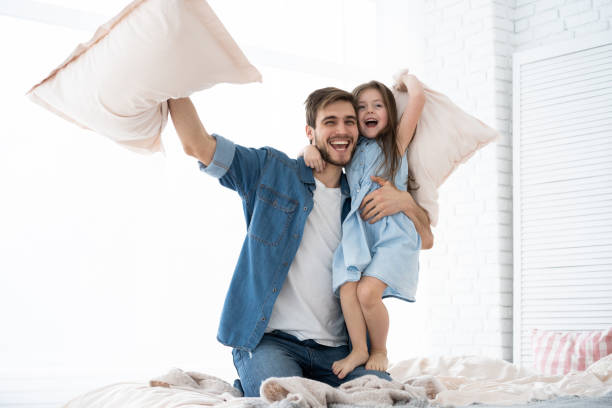 padre e hija feliz jugando pelea de almohadas en la cama por la mañana - lucha con almohada fotografías e imágenes de stock