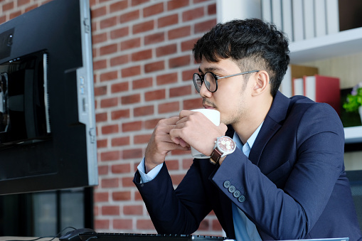 Young asian businessman concentrate on working with computer at office, Asian office man holding coffee cup while comtemplate on working with computer  business people and office male lifestyle concept