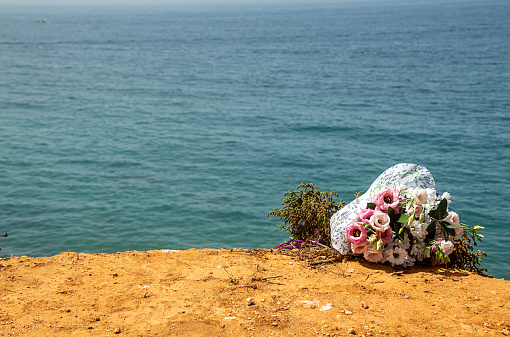 Funeral flowers at the beach. Flower bouquet on doom place, memory, Atlantic ocean, spanish seashoore. copy space,  Funeral symbol and Condolence card concept
