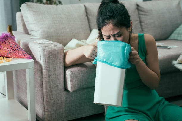 girl throw up in trash can after last night party tired exhausted asian japanese woman wearing fashion dress feeling unwell and suffering from nausea. young girl sitting on floor leaning on couch and throw up in trash can after last night party. vomiting stock pictures, royalty-free photos & images