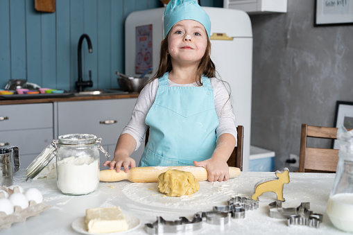 Little cute girl is cooking on kitchen. Having fun while making cakes and cookies. Smiling and looking at camera