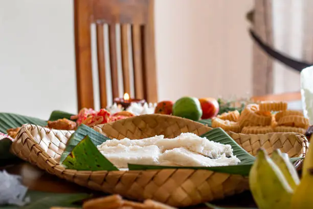 Shallow focused side view of Milk Rice (Kiribath), a Sinhala & Tamil New Year Avurudu festival food arranged on a banana leaf in a reed woven tray along with other traditional sweets in the background
