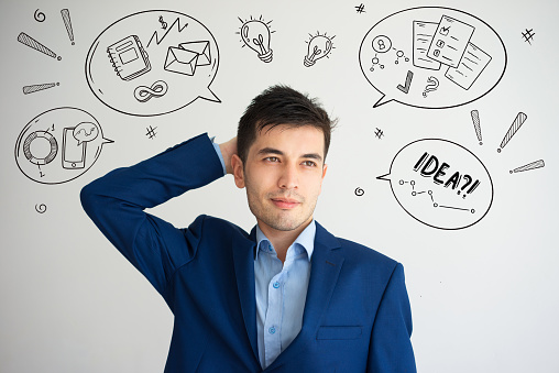 Relaxed man scratching head with hand drawn business sketches. Businessman looking away. Rest concept. Isolated front view on background with icons.