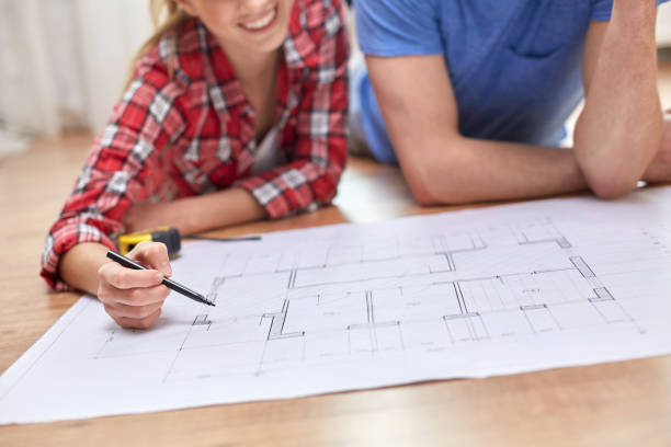 istock smiling couple looking at blueprint at home 1211767204