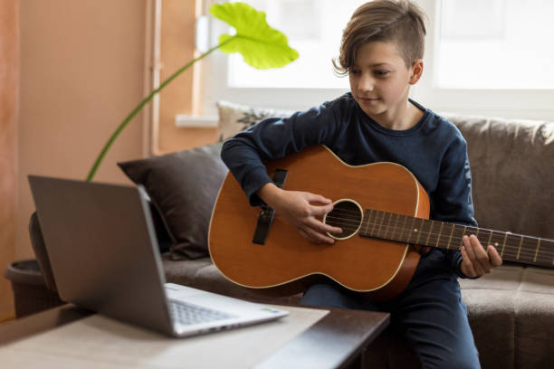 istock Smiling kid playing guitar and looking at laptop 1211768955