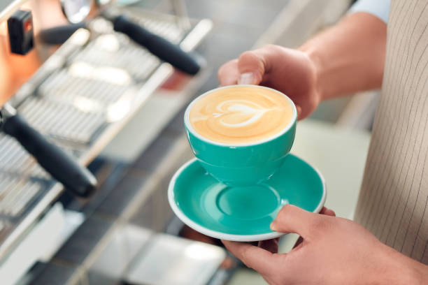 カフェで働く若い大人のバリスタ、手にコーヒーを持っている - barista coffee coffee crop heart shape ストックフォトと画像