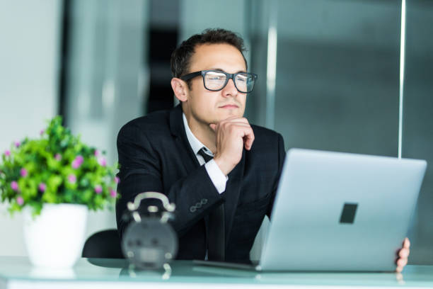 istock Young manager sitting at desk in office, working on laptop. 1211773967