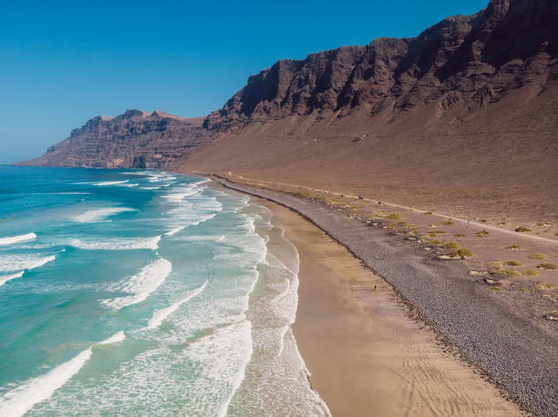 Aerial view of Famara beach, scenic landscape with ocean and mountains in Lanzarote, Canary islands Aerial view of Famara beach, scenic landscape with ocean and mountains in Lanzarote, Canary islands kite sailing stock pictures, royalty-free photos & images