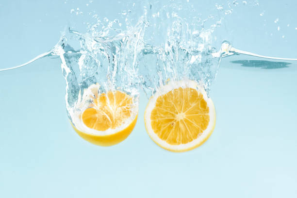istock Citrus splash. Lemon halves splattering into clear water on blue background 1211777556