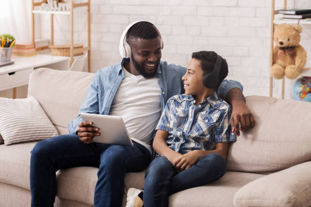 istock Afro Man And His Son In Wireless Headphones With Digital Tablet 1211777566