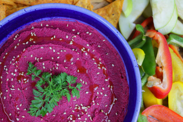 Close-up image of beetroot hummus platter, healthy vegan appetiser, Greek cuisine food (hommus / houmous) made from chickpeas, olive oil, tahini paste, roasted beetroot and garlic garnished with parsley and sesame seeds Stock photo showing a blue bowl of beetroot hummus garnished with flat leaf parsley and sesame seeds, healthy eating vegan appetiser, Greek cuisine food (hommus / houmous) made from chickpeas, olive oil, tahini paste, roasted beetroot and garlic. Served with Julienne carrot, cucumber, granny smith apple, nachos, peppers. appetiser stock pictures, royalty-free photos & images