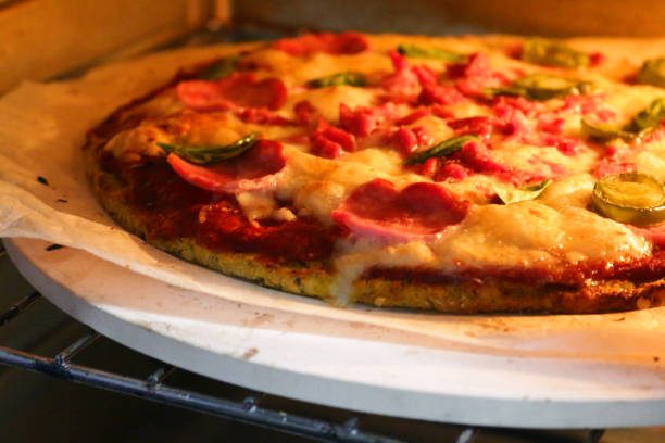 Image of cooked homemade pizza baking in oven, cooked on pizza stone for thin and crispy base, pepperoni and fresh basil leaves on top
