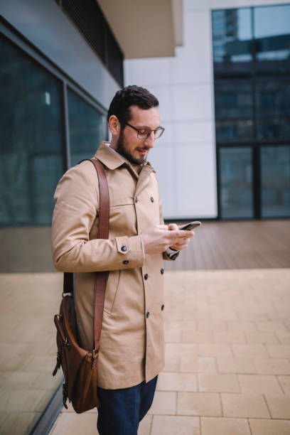 istock Man using mobile phone while walking on street to office 1211781948