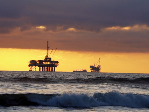 une belle vue de huntington beach of the sun setting over an oil, drill rig platform offshore - oil rig sea drill petroleum photos et images de collection