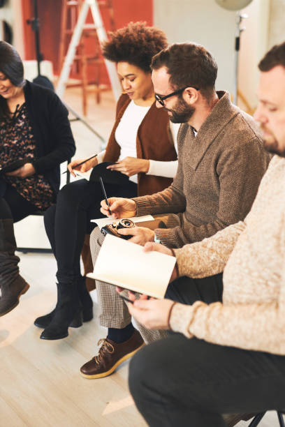 istock Multicultural group of attendees sitting in studio and writing notes about photography basics. 1211789526