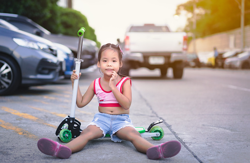 Cute little asian girl playing a scooter on the street