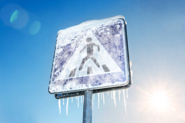 Frozen pedestrian sign covered with icicles in bright sun and blue sky