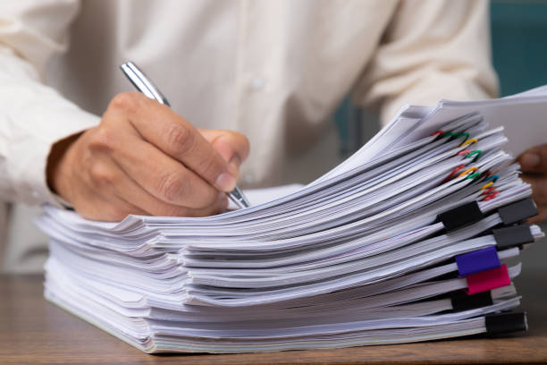 istock Male office workers with yellow shirt holding and writing documents on office desk, Stack of business overload paper. 1211804653