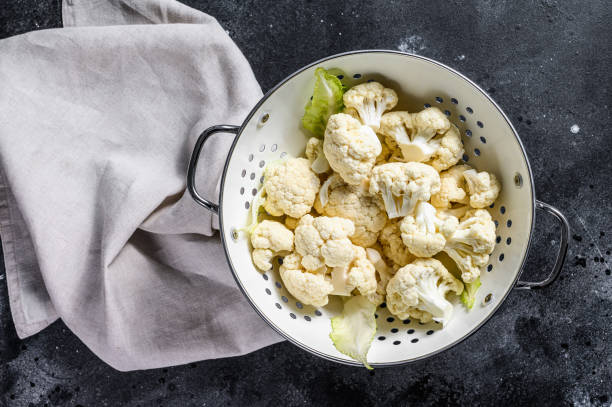 istock Fresh white heads cleaned cauliflower in a colander. Black background. Top view 1211804905