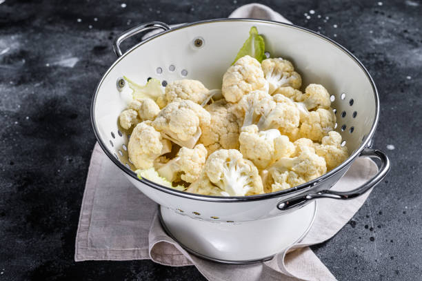 istock Fresh white heads cleaned cauliflower in a colander. Black background. Top view 1211804931