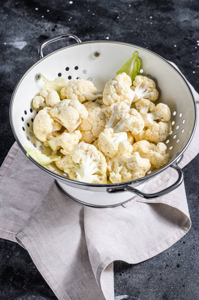 istock Fresh white heads cleaned cauliflower in a colander. Black background. Top view 1211804957